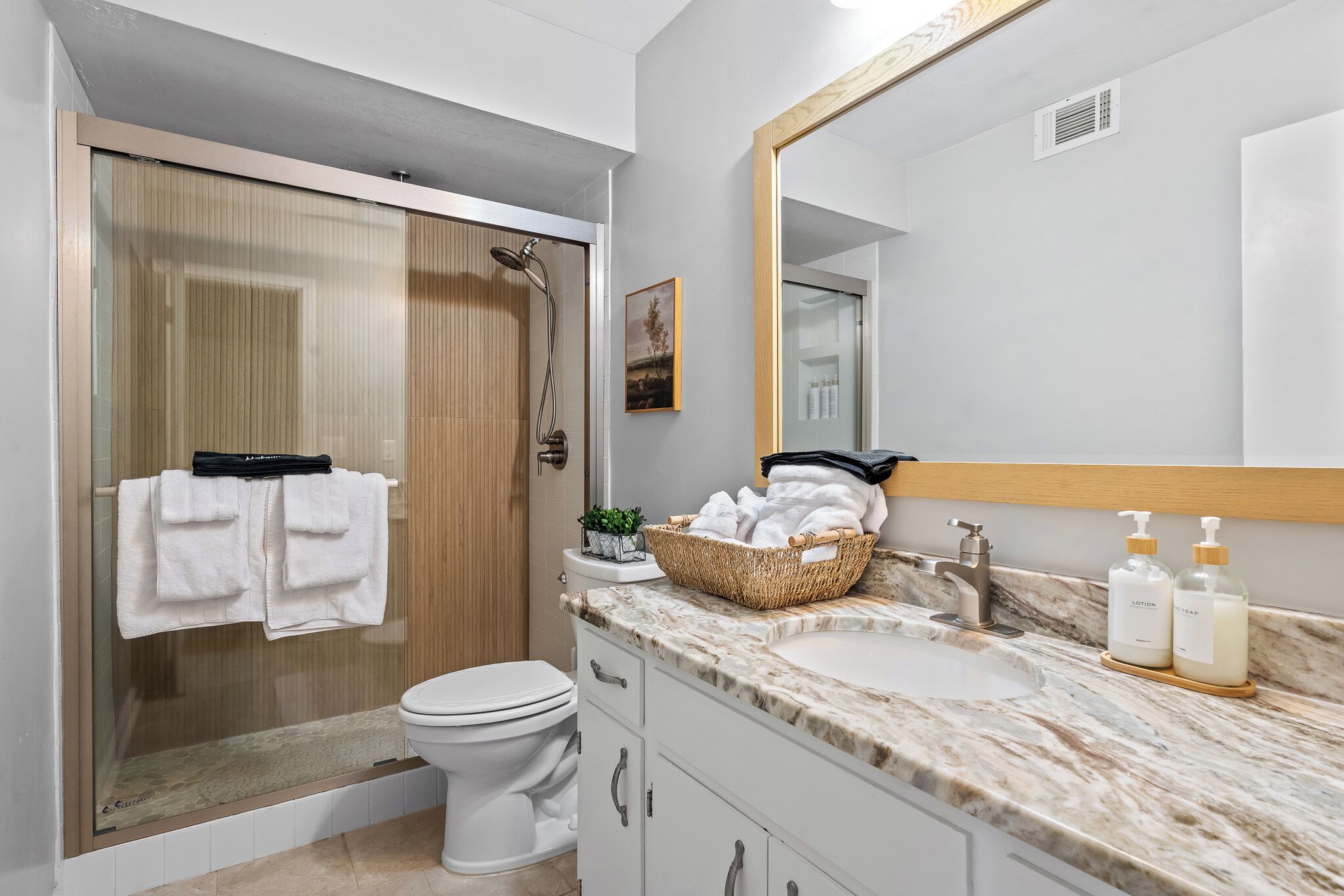 Une salle de bain moderne avec une douche à parois de verre, des toilettes, un lavabo avec un plan de travail en marbre et un grand miroir.