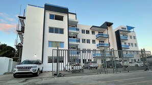 A multi-story building with balconies, a gated entrance, and a white SUV parked in front.
