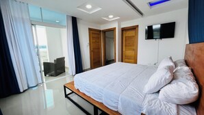 A modern bedroom with a large bed, wooden doors, a flat-screen TV, and a view through a glass door.