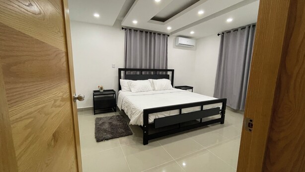 A bedroom with a bed, a nightstand, a small table, and a grey rug.