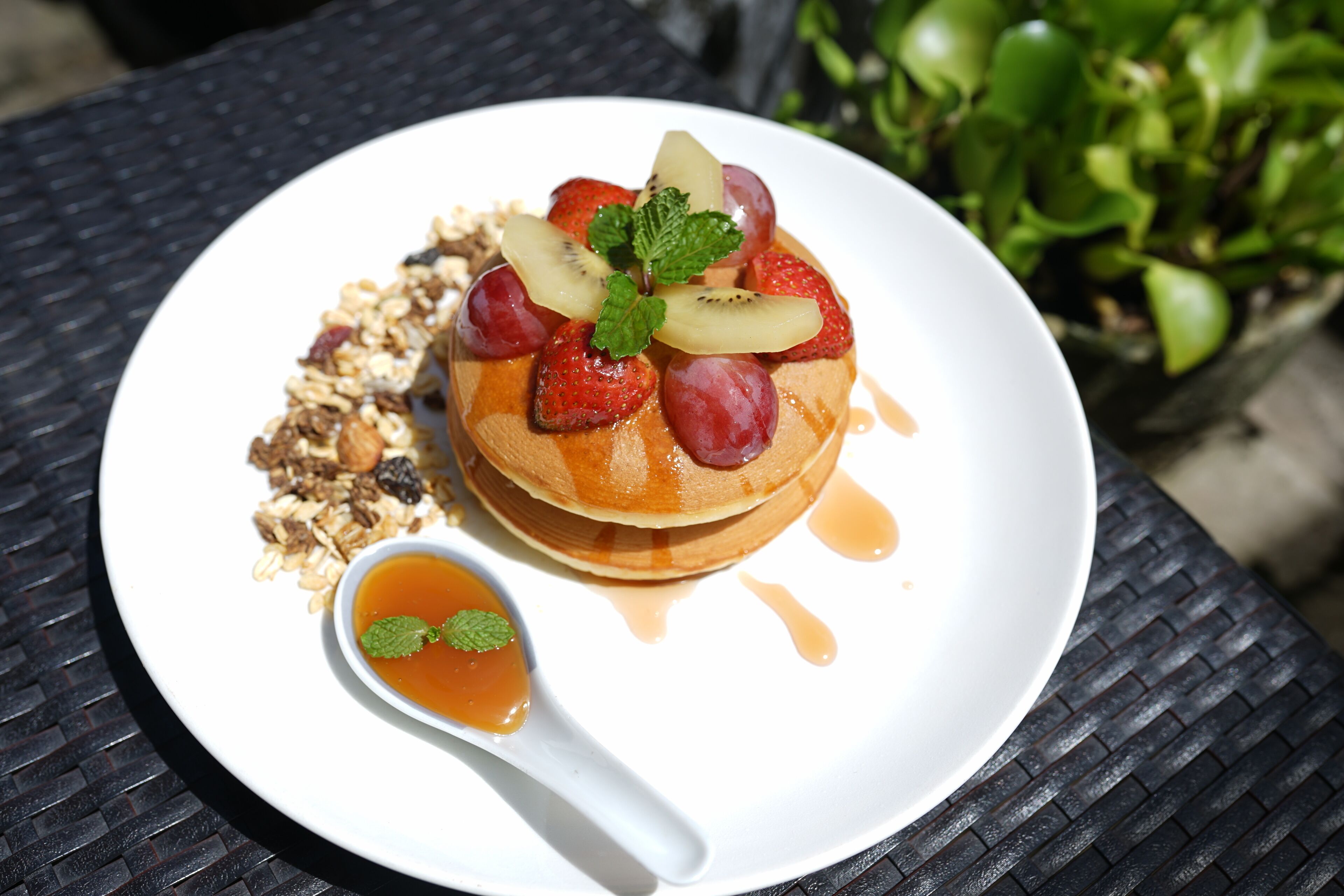 A breakfast plate with pancakes, fruit, and syrup on a table.