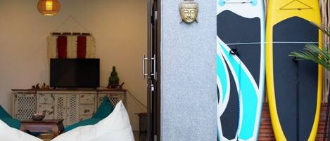 A room with a sofa, cushions, a television, and a Buddha statue. There are two surfboards leaning against the wall.