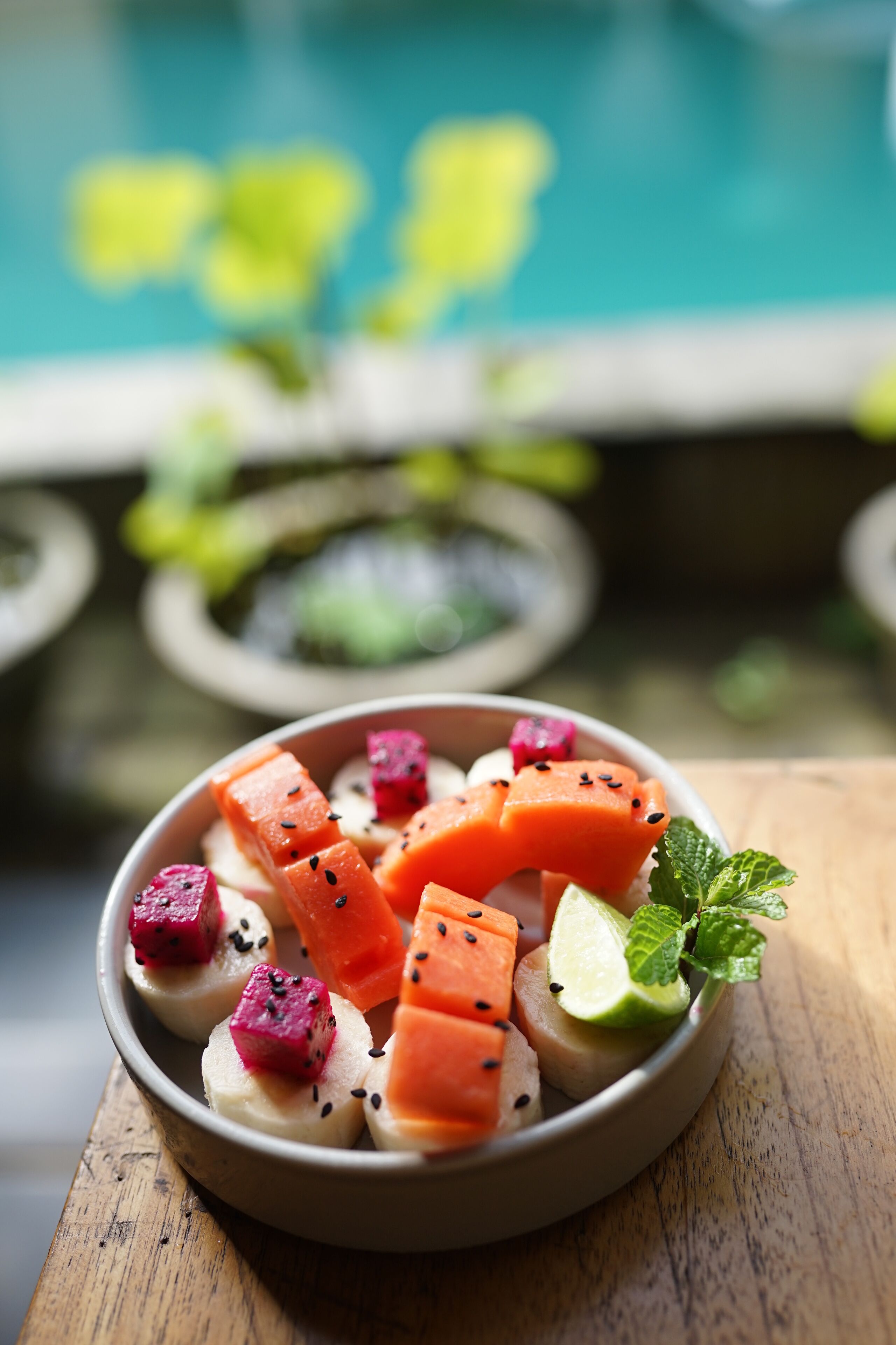 A bowl of fruit on a wooden table with a blurred outdoor background.