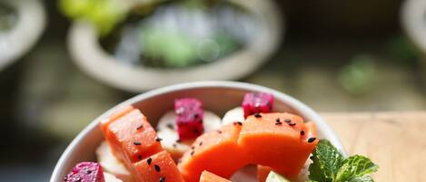 A bowl of fruit on a wooden table with a blurred outdoor background.