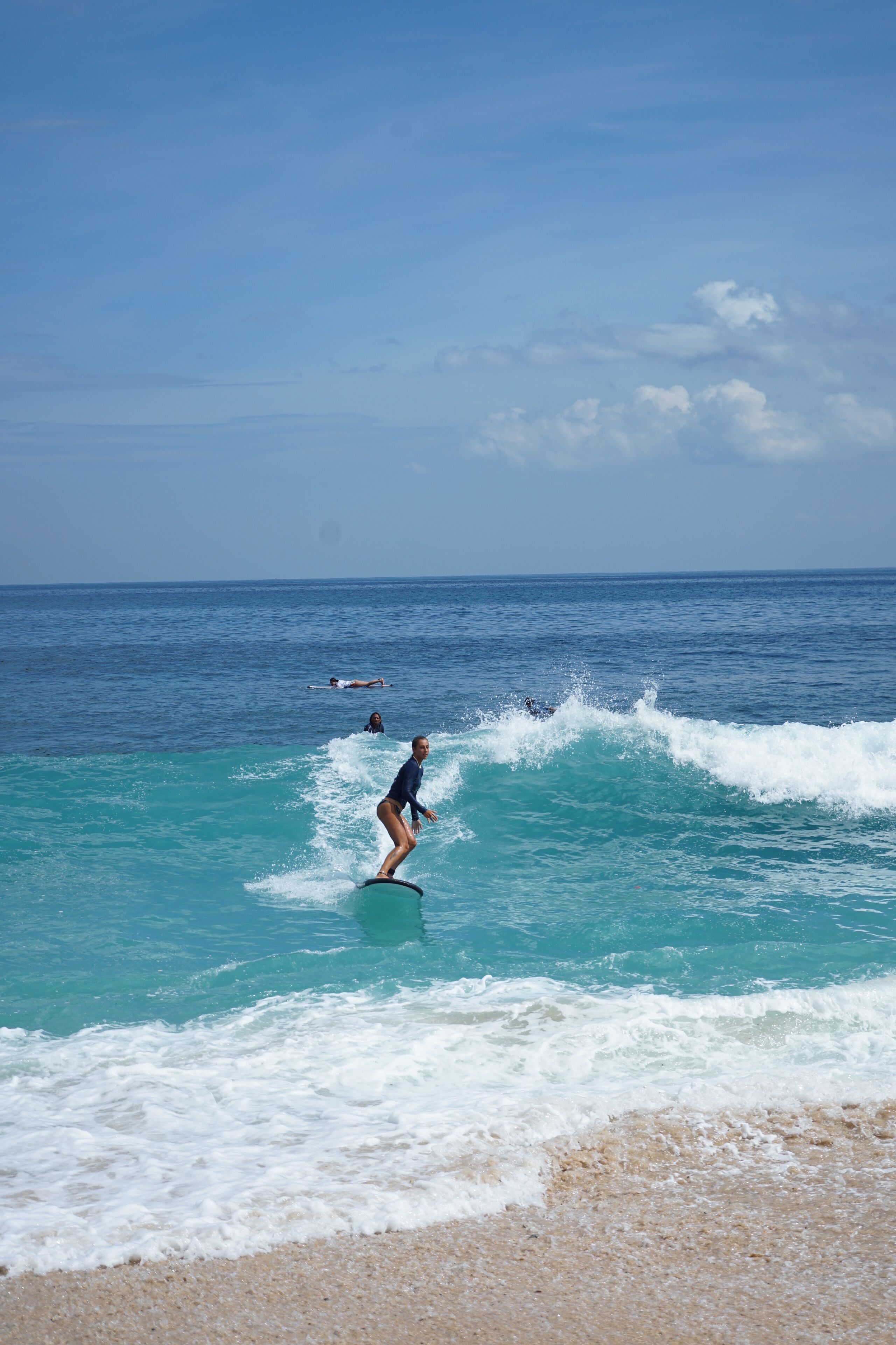 A beach with clear blue water and a person surfing.