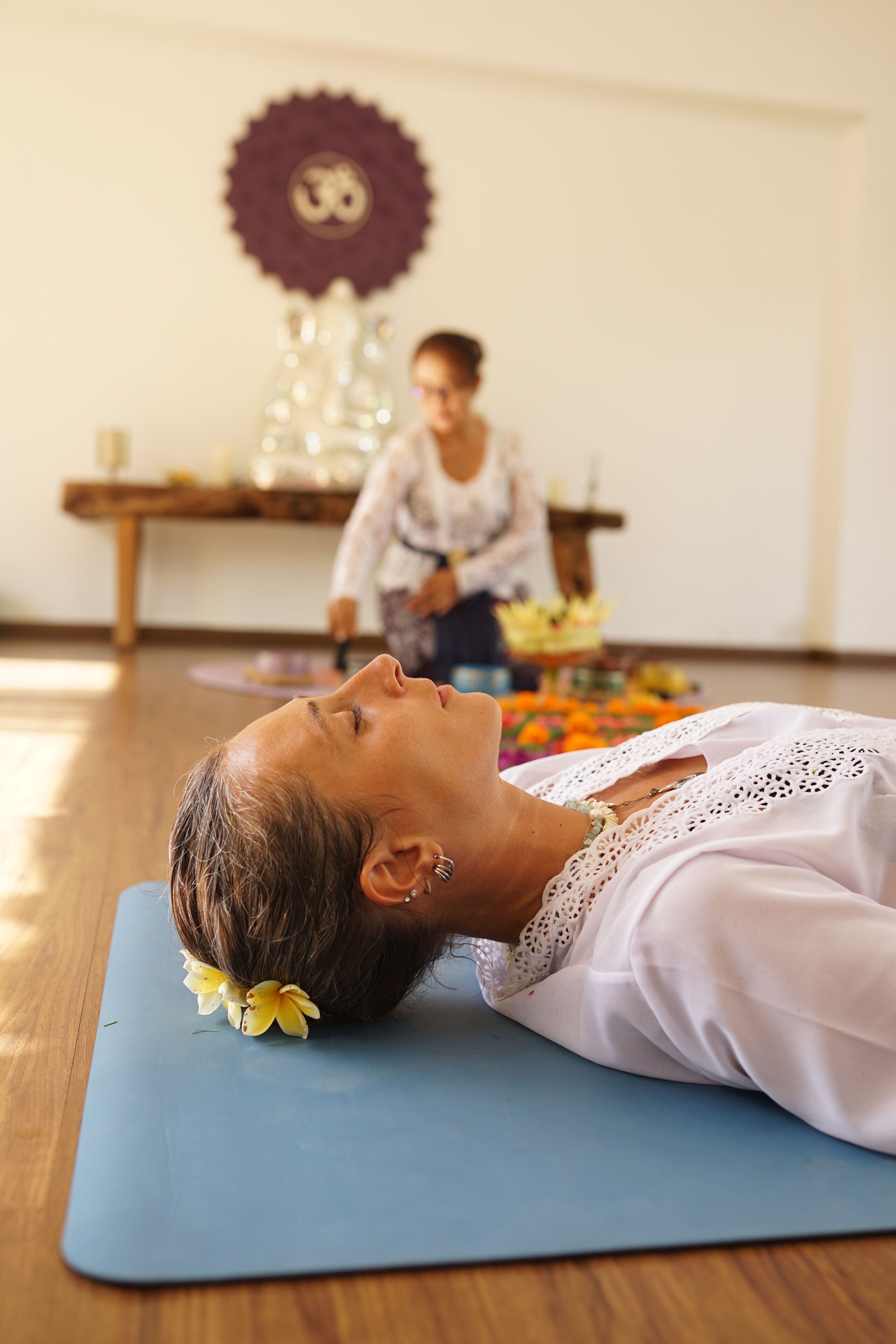 A person lying on a yoga mat in a room with a wooden floor and a decorative wall piece.