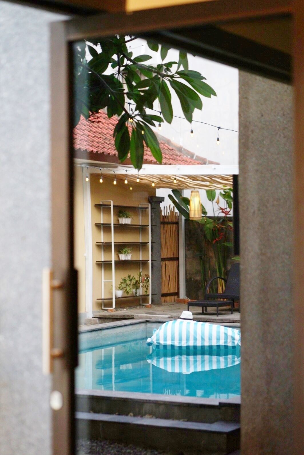 Vista a través de una puerta de vidrio a un patio trasero con piscina, zona de estar cubierta y valla de madera.