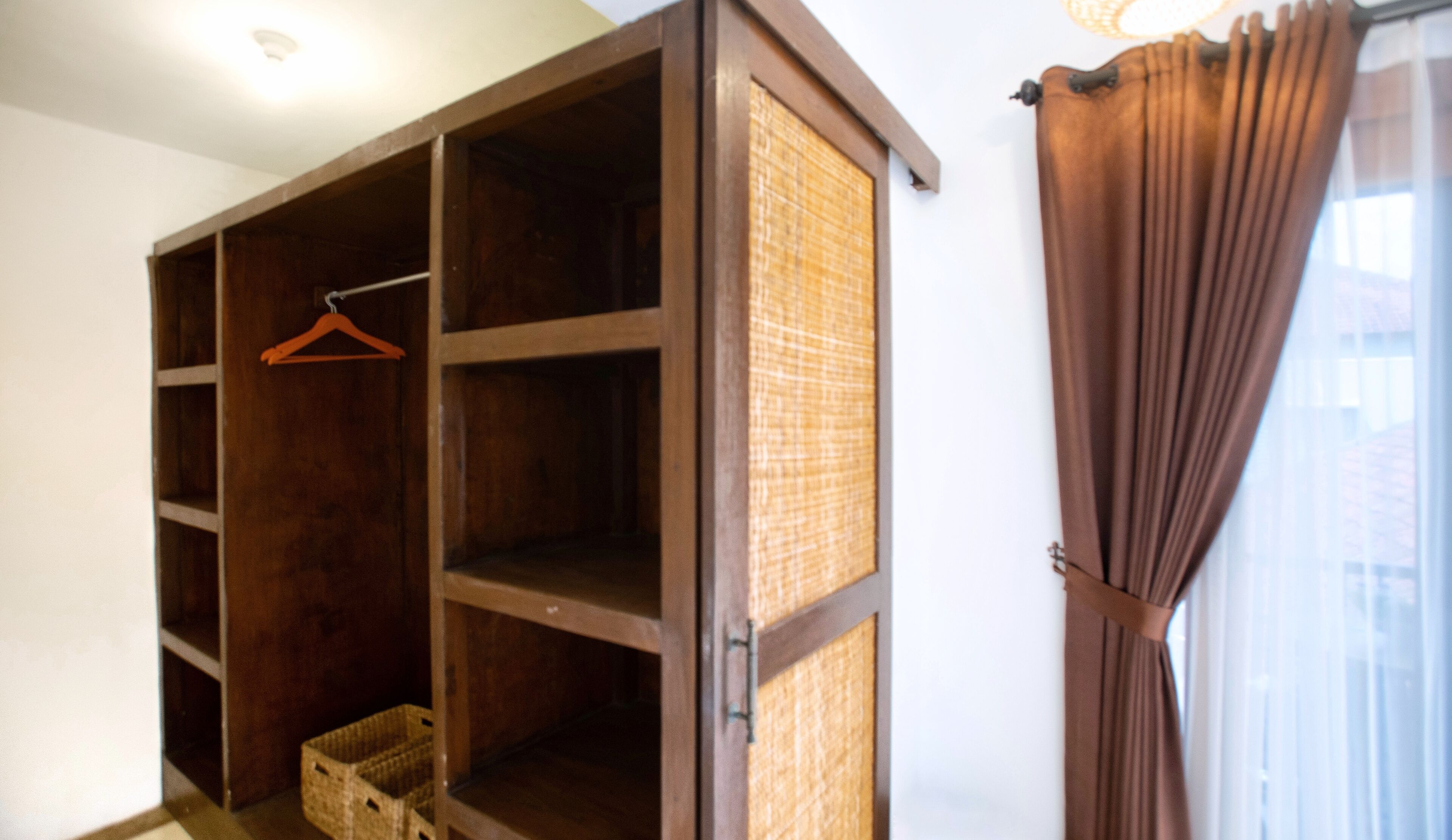 A room with a wooden wardrobe, a wicker basket, and a brown curtain.
