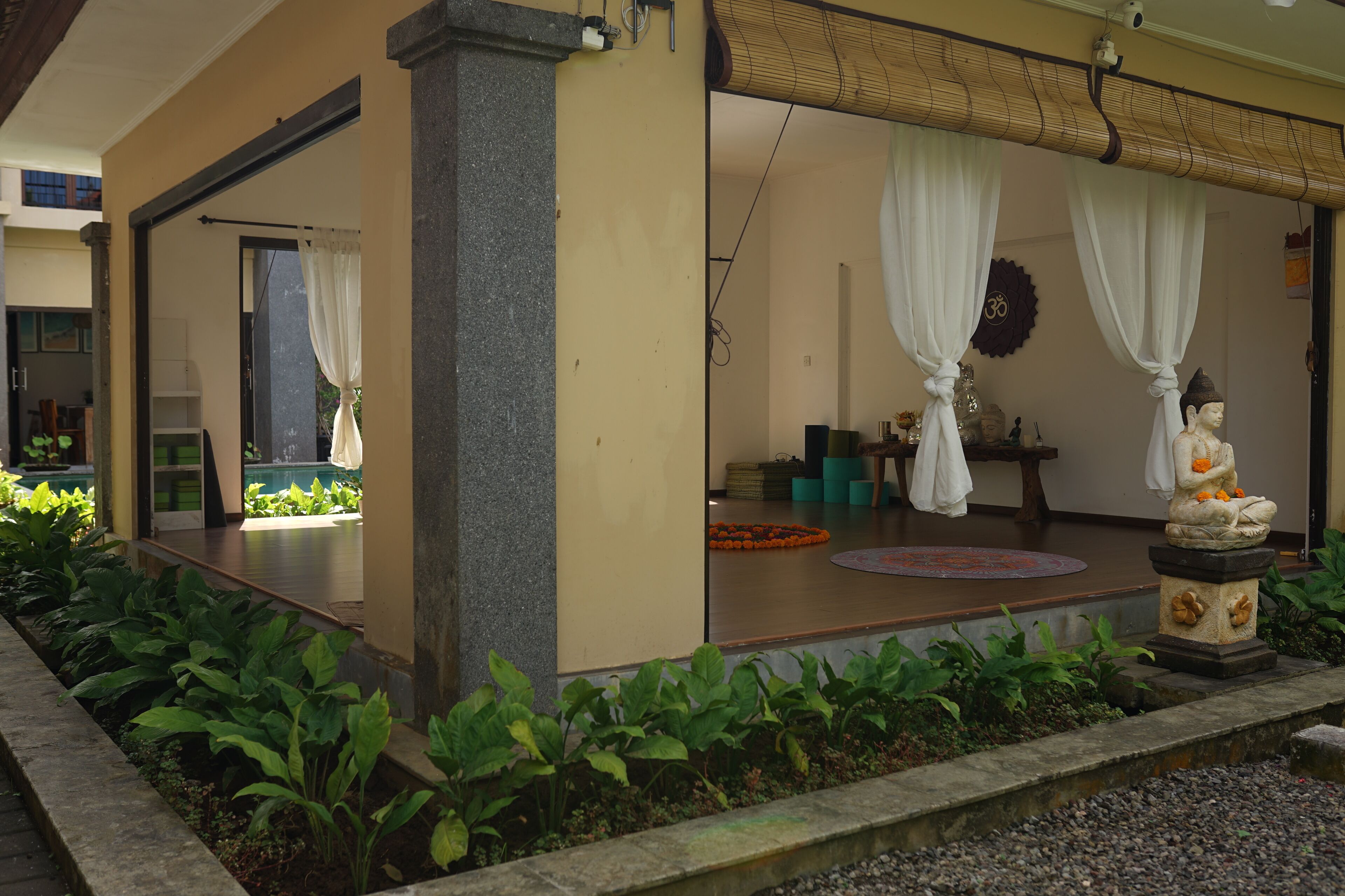 Un jardín interior tranquilo con una estatua, un banco de piedra y un pequeño altar con flores.