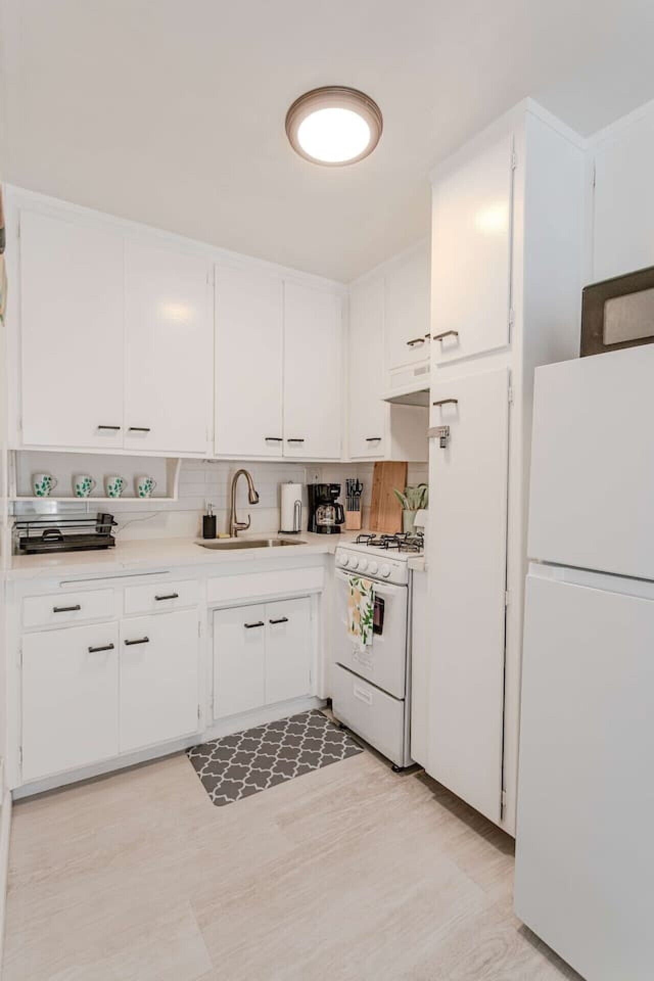 A modern kitchen with white cabinetry, a gas stove, a refrigerator, and a patterned rug.