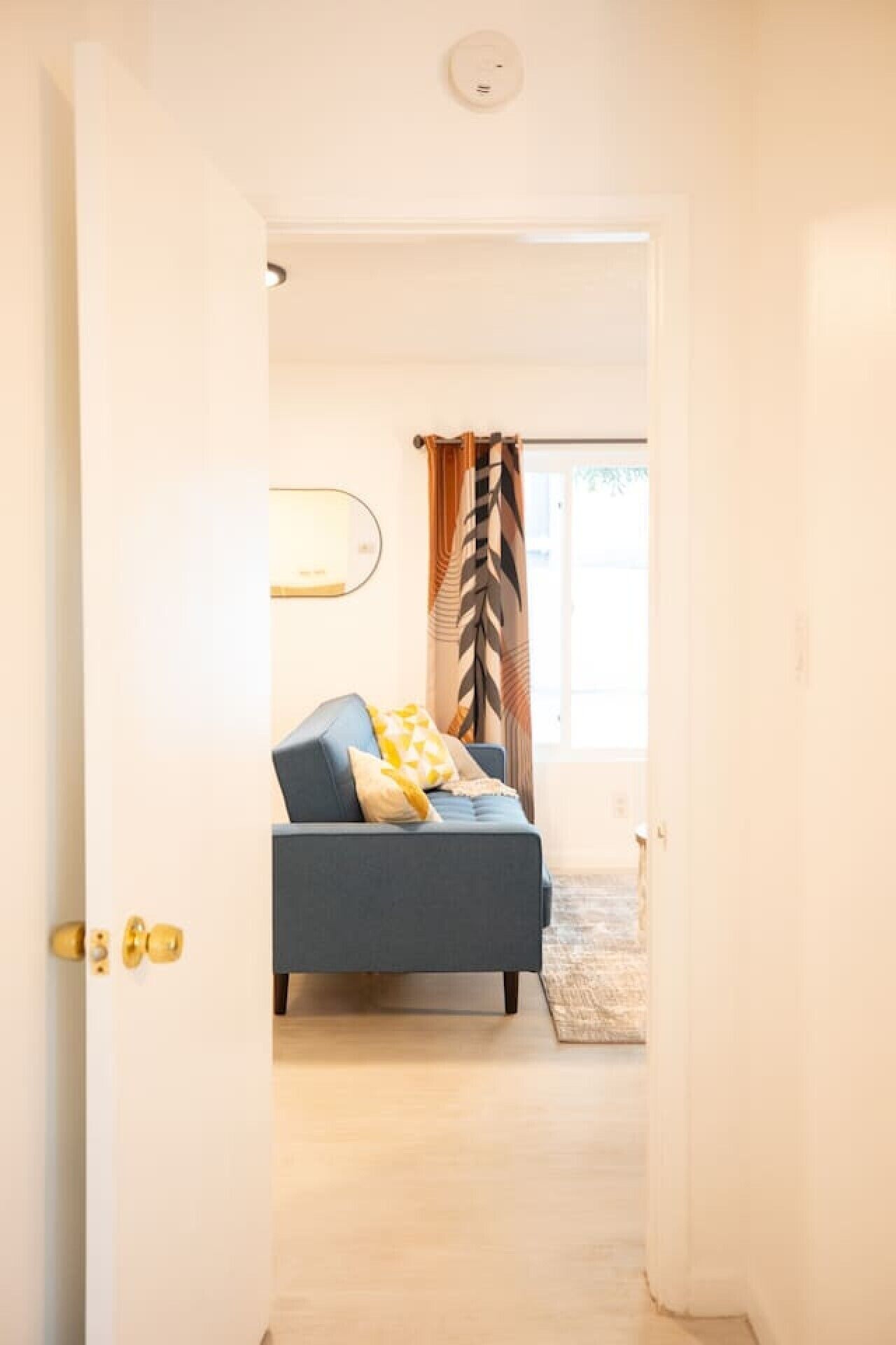 A doorway leading to a bedroom with a bed, a bedside table, and a window with curtains.