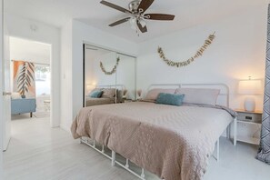 A bedroom with a bed, bedside tables, a ceiling fan, and a mirror. - King Suite | Walk to Beach | Patio + Parking (Oceanside)