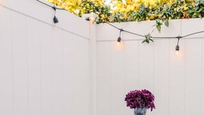 Un tavolo apparecchiato con piatti e un vaso di fiori, circondato da un muro bianco e luci a stringa.
