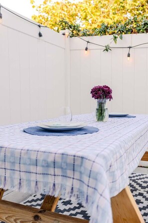 A table set with plates and a vase of flowers, surrounded by a white wall and string lights. - King Suite | Walk to Beach | Patio + Parking (Oceanside)