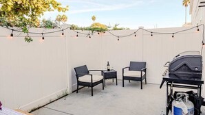 Un'area patio all'aperto con due sedie, un barbecue e un tavolo con un sottotavolo.
