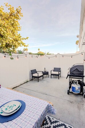 An outdoor patio area with two chairs, a grill, and a table with a placemat. - King Suite | Walk to Beach | Patio + Parking (Oceanside)