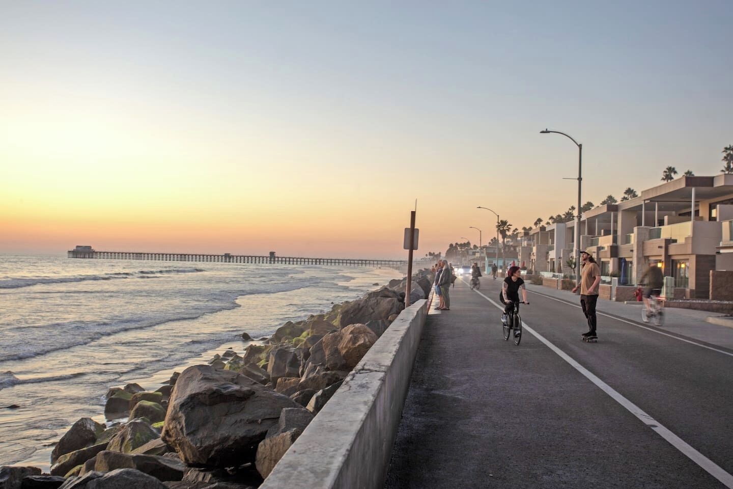 A coastal road with a bike lane, a pedestrian path, and a pier in the distance.