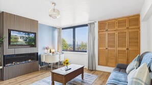 A living room with a TV, a wooden cabinet, a sofa, and a large window with curtains.