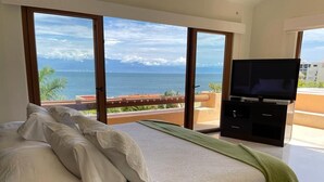 Un dormitorio con cama, televisor y balcón con vistas al océano.
