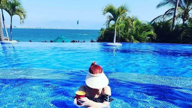 Una persona sentada en una piscina con vistas al mar y palmeras.