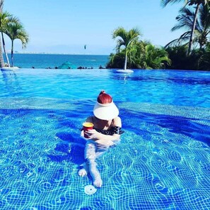 A person sitting in a swimming pool with a view of the sea and palm trees. - Welcome to your home in wonderful Punta Esmeralda! Ready to relax & have fun?  (Nayarit)