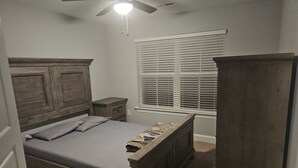 A bedroom with a wooden bed, a nightstand, a wardrobe, a ceiling fan, and a window with blinds.