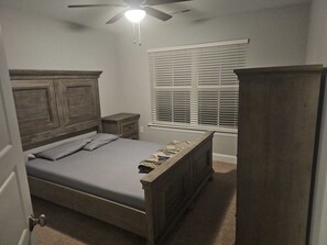A bedroom with a wooden bed, a nightstand, a wardrobe, a ceiling fan, and a window with blinds. - Spacious 5-bedroom house in delightful North Raleigh with AC, WiFi. (Raleigh)
