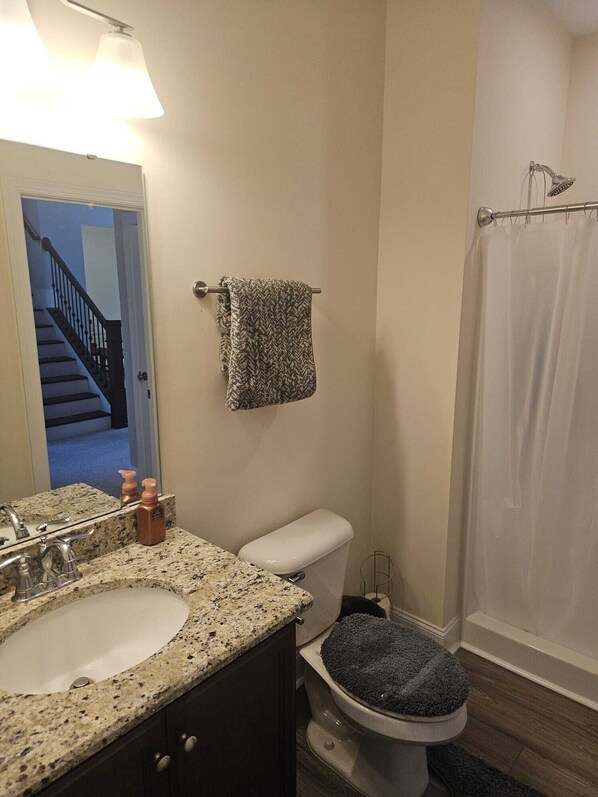 A bathroom with a granite countertop sink, a toilet with a blue seat cover, a shower curtain, and a towel hanging on a metal rod. - Spacious 5-bedroom house in delightful North Raleigh with AC, WiFi. (Raleigh)