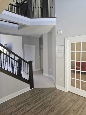 A multi-level interior with a staircase, a door with a frosted glass panel, and a sign with the text "Be all you can be KIND". - Spacious 5-bedroom house in delightful North Raleigh with AC, WiFi. (Raleigh)