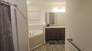 A bathroom with a bathtub, a sink, and a mirror. There is a shower curtain and a door handle visible.