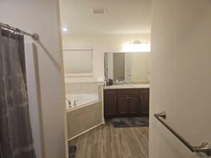 A bathroom with a bathtub, a sink, and a mirror. There is a shower curtain and a door handle visible. - Spacious 5-bedroom house in delightful North Raleigh with AC, WiFi. (Raleigh)