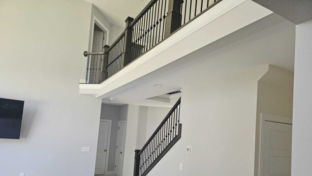 A spacious living room with a high ceiling, a black leather chair, and a staircase with a black railing.