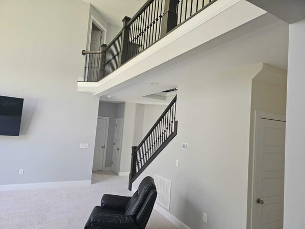 A spacious living room with a high ceiling, a black leather chair, and a staircase with a black railing. - Spacious 5-bedroom house in delightful North Raleigh with AC, WiFi. (Raleigh)