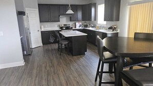 A modern kitchen with dark cabinets, a central island, and a dining area with a large table and chairs.
