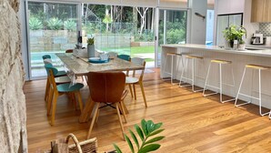 Une cuisine moderne dotée d’un coin bar, de grandes fenêtres et d’un espace repas avec un plancher et des chaises en bois.