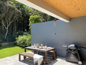 Une terrasse extérieure avec une table en bois dressée pour les repas, un barbecue et un espace salon abrité.