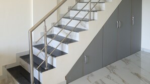 A staircase with a metal railing, marble steps, and grey cabinets.