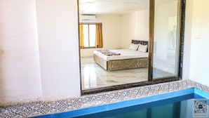 A bedroom with a large mirror, a bed, and a view of another room.