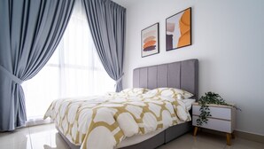 A modern bedroom with a grey upholstered bed, a white bedside table with a plant, and two abstract art pieces on the wall. - Trion Suites KL By DSM (Kuala Lumpur)