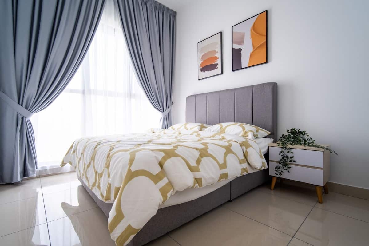Un dormitorio moderno con una cama tapizada de gris, una mesita de noche blanca con una planta y dos obras de arte abstracto en la pared.