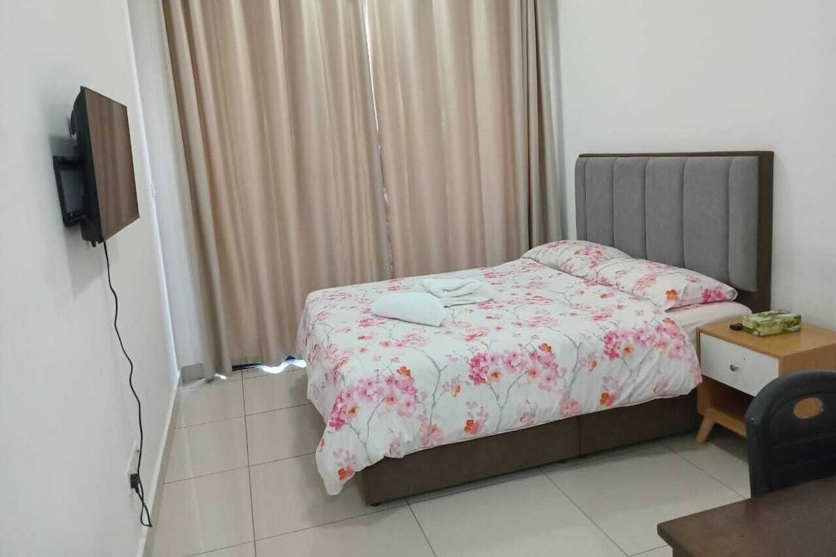 Un dormitorio ordenado con cama, mesita de noche, silla y televisor montado en la pared.