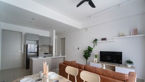 A modern kitchen with a built-in oven and a dining area with a brown sofa and a TV. - Trion Suites KL By DSM (Kuala Lumpur)
