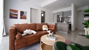A modern living room with a brown sofa, a round wooden coffee table, and a kitchen in the background. - Trion Suites KL By DSM (Kuala Lumpur)