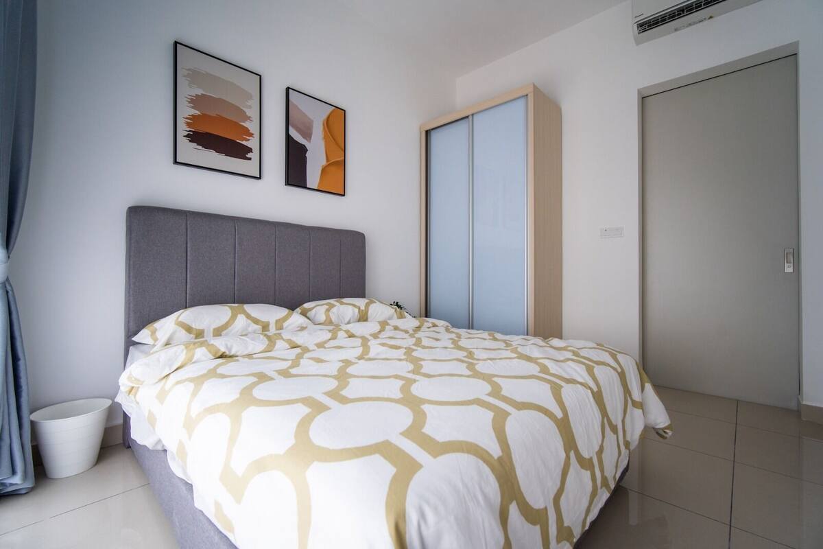 Un dormitorio con cama, cabecera gris, armario y dos cuadros enmarcados en la pared.