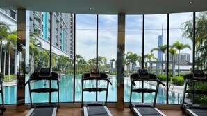 A gym with treadmills and a large window overlooking a swimming pool and cityscape. - Trion Suites KL By DSM (Kuala Lumpur)