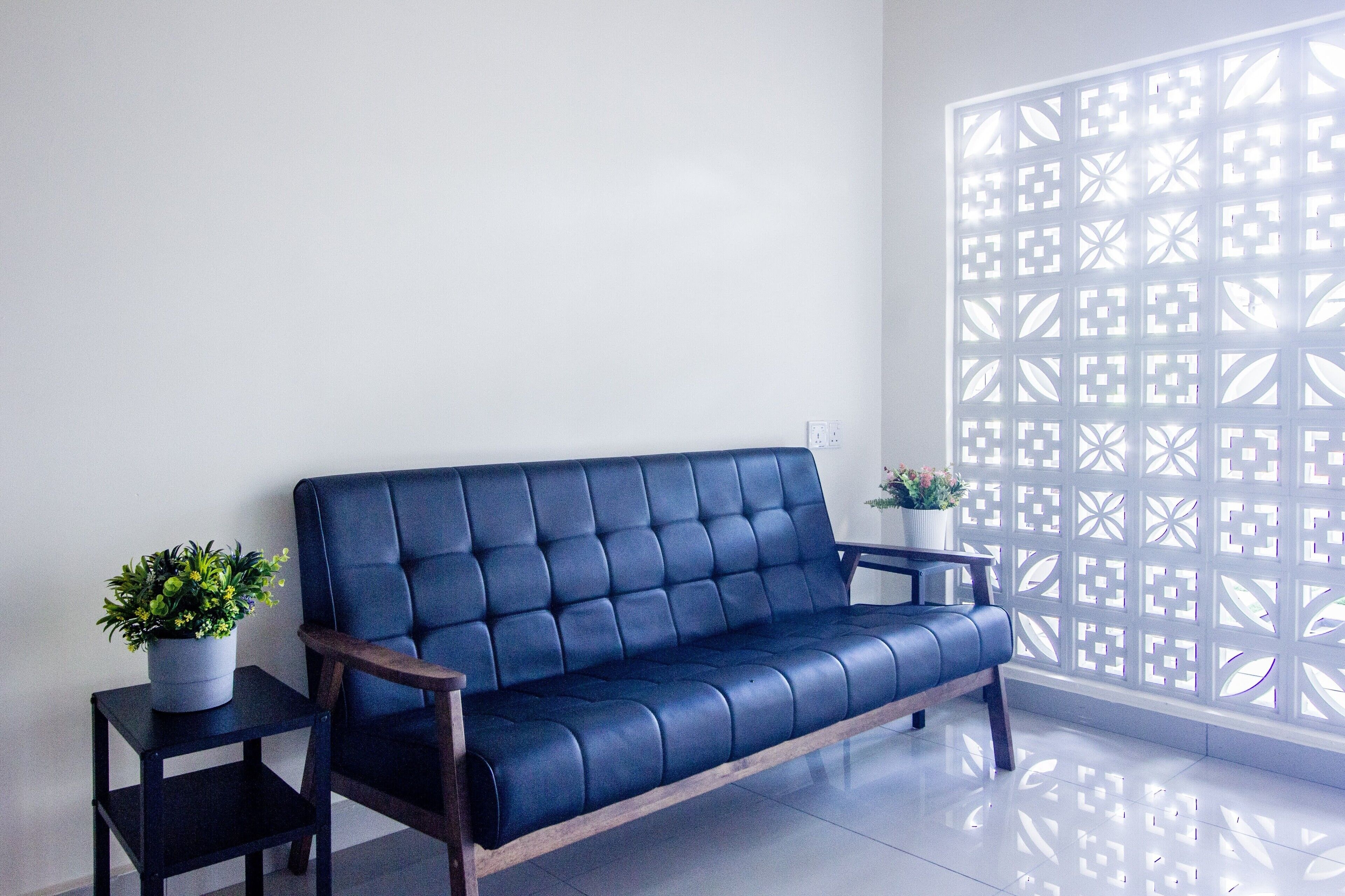 Un sofá azul con reposabrazos de madera, una mesita auxiliar con una planta en maceta y un separador decorativo con diseños geométricos.