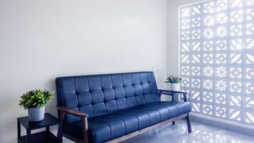Un sofá azul con reposabrazos de madera, una mesita auxiliar con una planta en maceta y un separador decorativo con diseños geométricos.