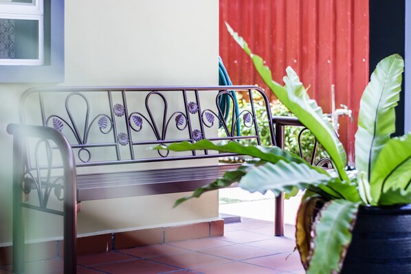 A metal bench with decorative patterns, a potted plant, and a red wall in the background. - Plumeria 4BR Garden House by uBook (Butterworth)