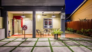 A modern house with a patio area featuring a dining table and chairs, a potted plant, and a red and white gate. - Plumeria 4BR Garden House by uBook (Butterworth)