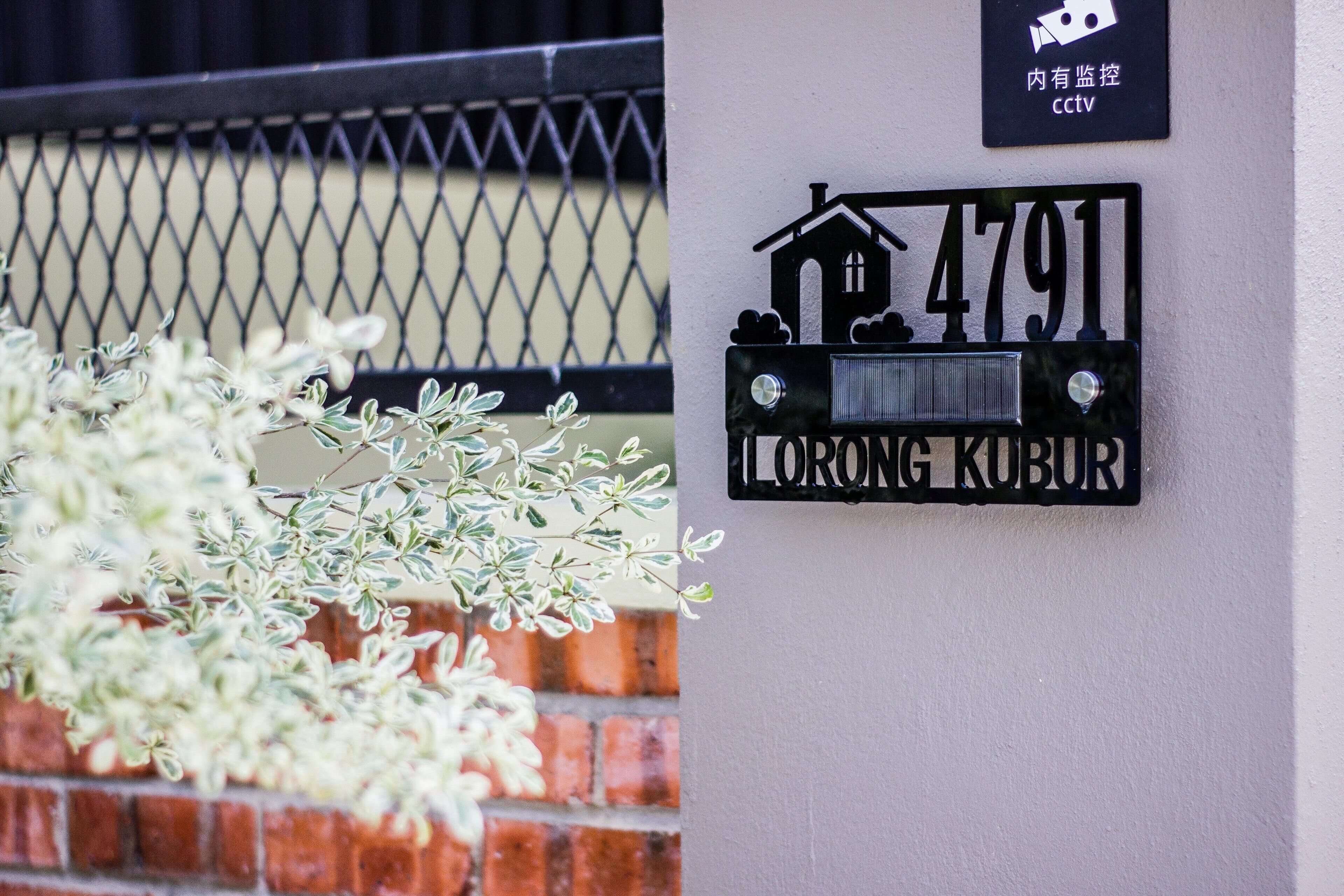 A house number sign with a house icon and the text "4791 LORONG KUBUR" on a white wall.